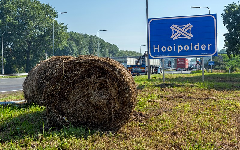 Bord van knooppunt Hooipolder langs de snelweg met daarvoor een opgerolde hooibaal in het gras