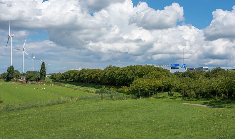 De A27 vanuit de verte. Op de voorgrond weiland met bomen en windmolens